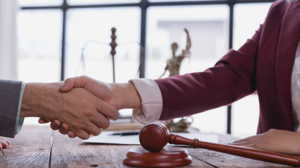 Ein Mann und eine Frau reichen sich die Hände, im Vordergrund liegt ein Richterhammer
