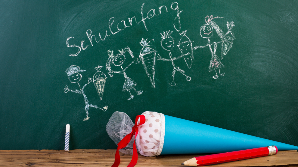 blaue Schultüte liegt vor einer Kreidetafel auf der der Schriftzug Schulanfang zu lesen ist