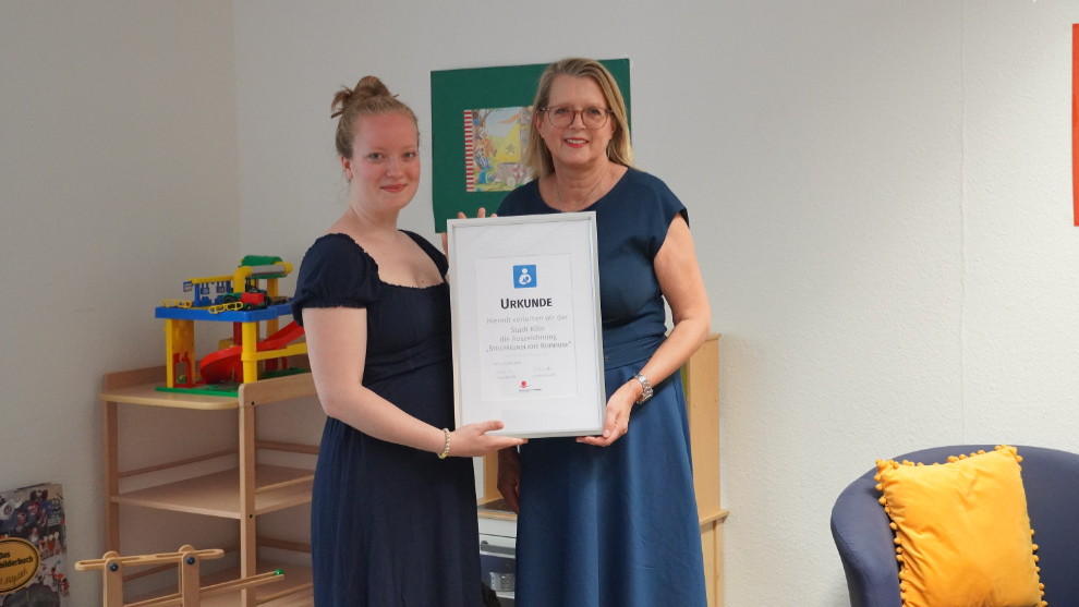 Links steht Lea Milz, erste Kreissprecherin des Kreises Köln-Rhein-Erft-Kreis des Landesverbands der Hebammen NRW e. V., sie übergibt Stadtdirektorin Andrea Blome (rechts) die Urkunde