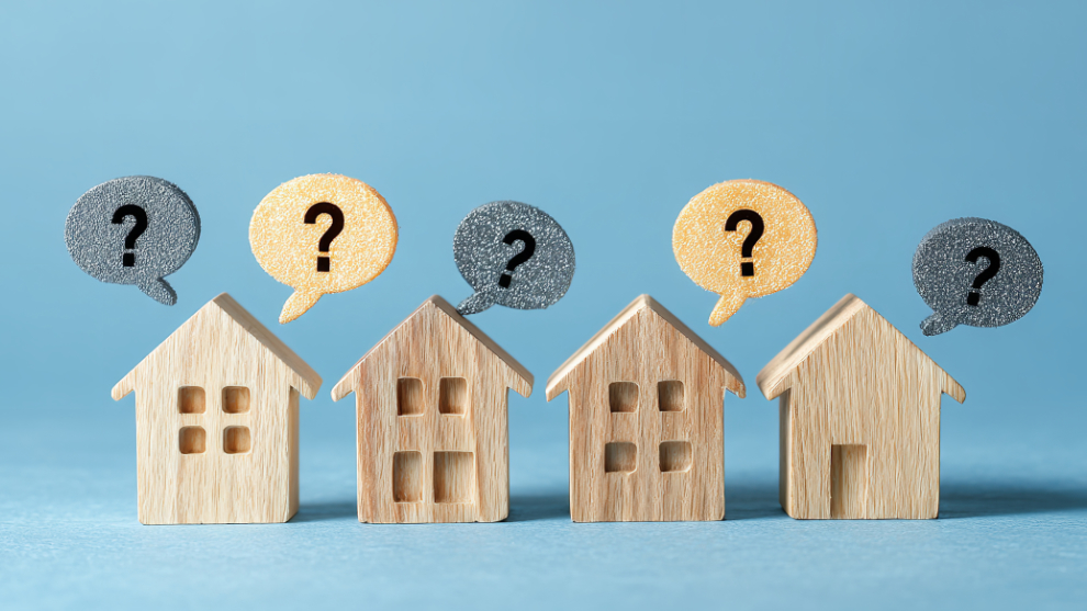 Vier kleine Holzhäuser in einer Reihe stehend mit Sprechblasen darüber, in denen Fragezeichen eingetragen sind.