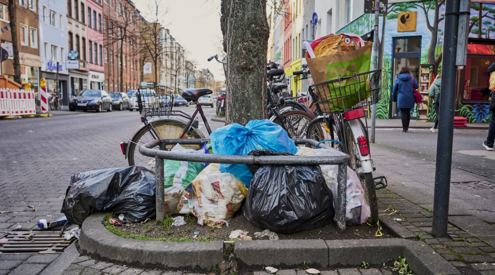 Mehrere große Mülltüten liegen an einer Baumscheibe. Dahinter stehen Fahrräder.