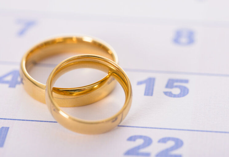 Zwei goldene Trauringe liegen auf einem Kalenderblatt, © Smarterpix/Andrey Popov