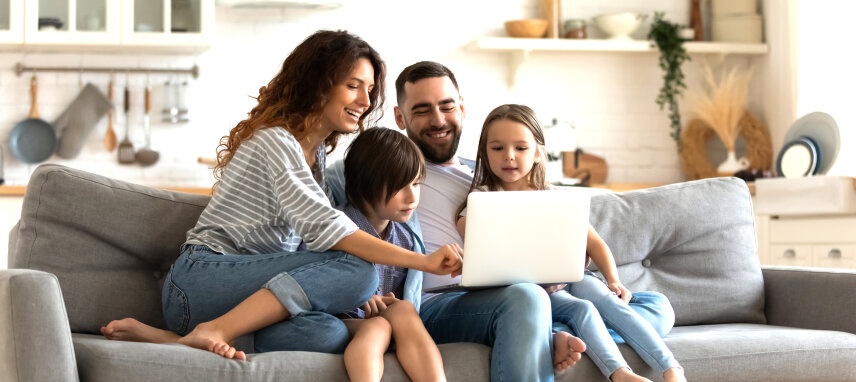 Vater, Mutter und zwei Kinder sitzen auf einer Couch und schauen auf ein Laptop
