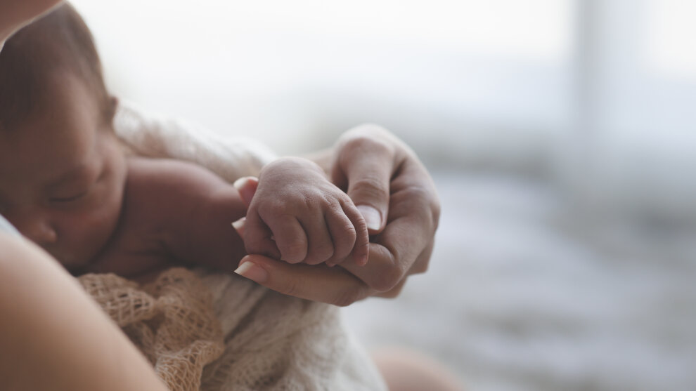Nahaufnahme einer Mutter, die die Hände ihres Neugeborenen hält.