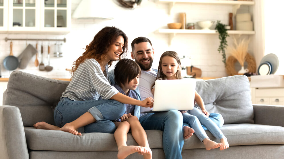 Vater, Mutter und zwei Kinder sitzen auf einer Couch und schauen auf ein Laptop