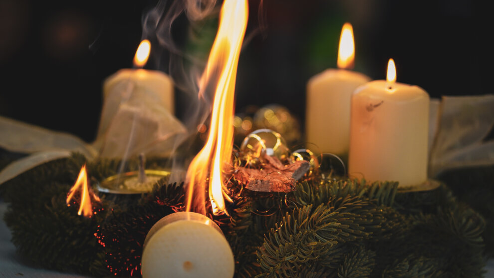 Adventskranz mit vier Kerzen. Eine Kerze ist umgekippt und der Adventskranz fängt an zu brennen.