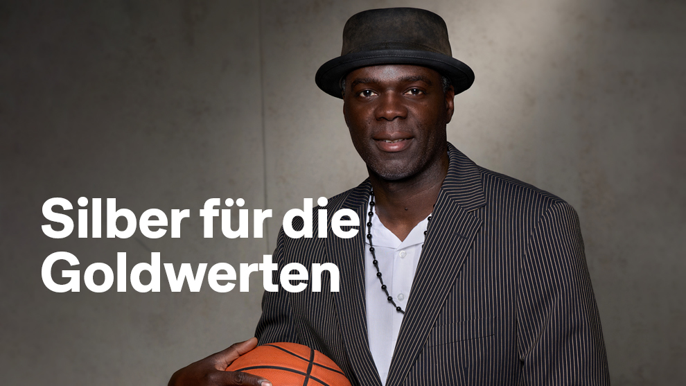 Ein Mann hält einen Basketball in der Hand. Links von ihm steht der Schriftzug "Silber für die Goldwerten"