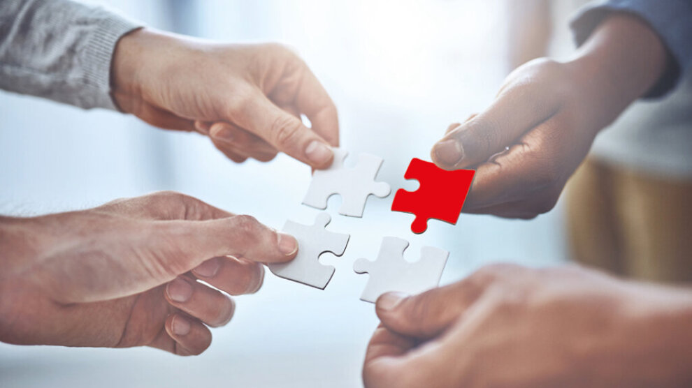 Vier Hände halten vier Puzzleteile, drei weiß, eins rot