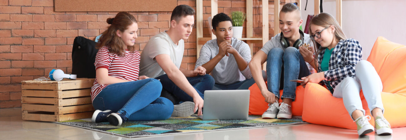 Gruppe Jugendlicher verbringen gemeinsam Zeit miteinander, sitzend auf dem Boden und Sitzsäcken.