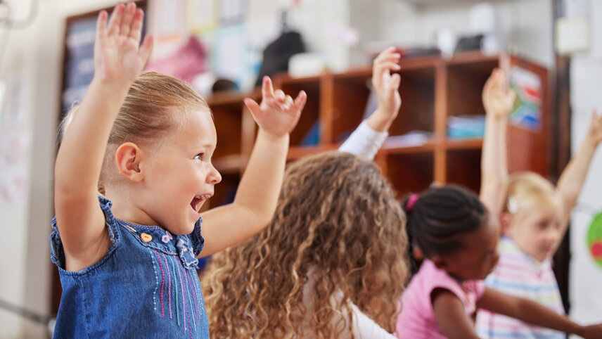Kindergartenkinder heben strahlend die Hände in die Höhe