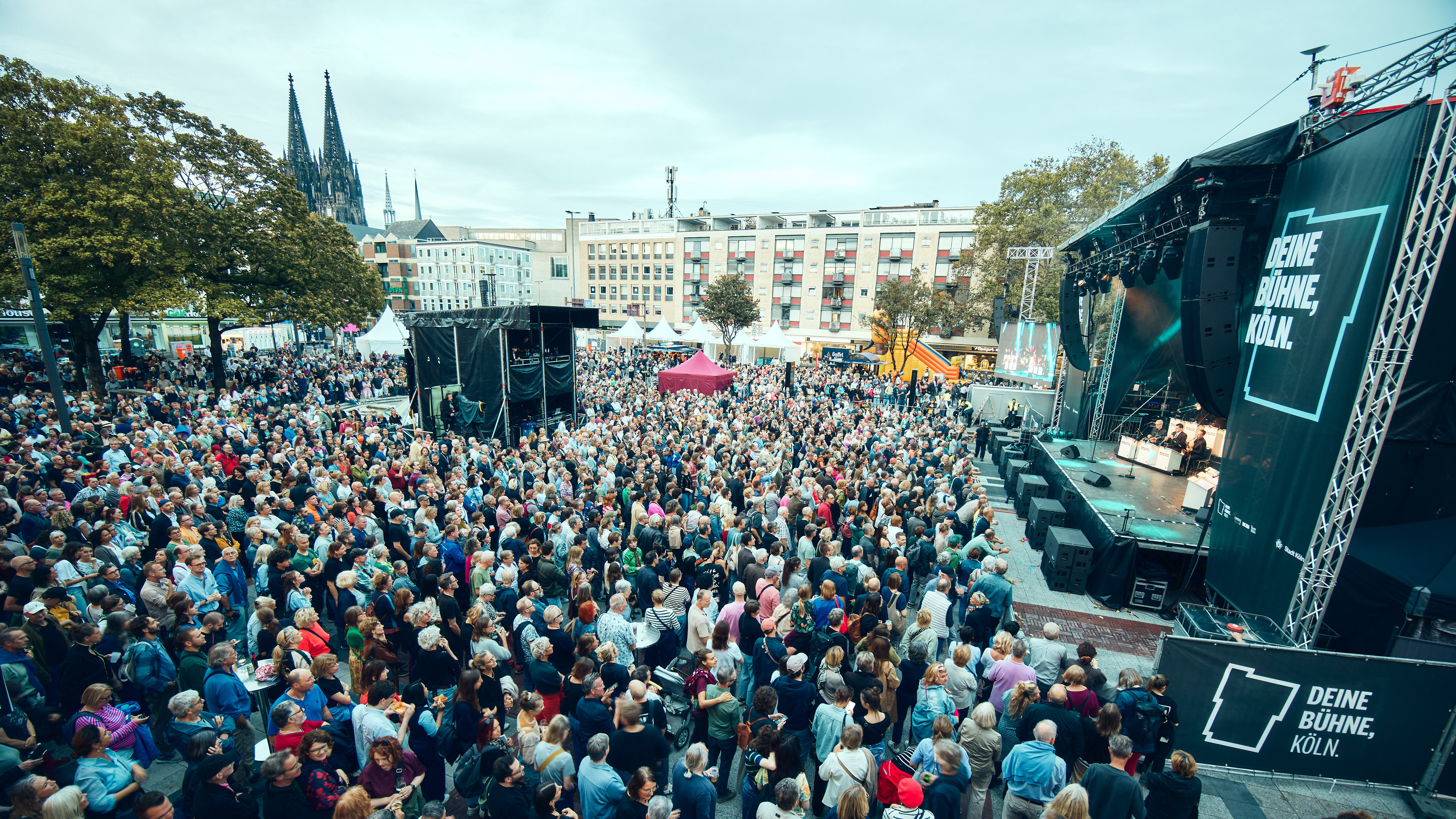 Eine Menschenmenge steht vor einer Bühne, die vor dem Opernhaus aufgebaut ist, im Hintergrund sieht man den Dom
