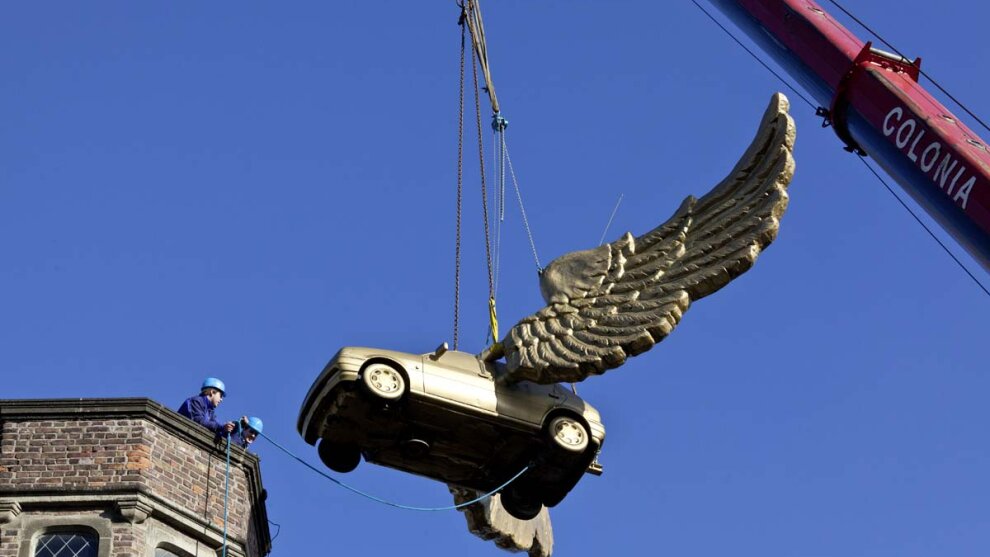 Geflügeltes Auto hängt an einem Kran vor dem Turm des Zeughauses.