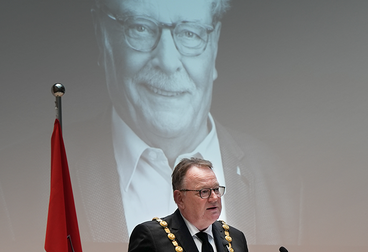Oberbürgermeister Torsten Burmester steht an einem Rednerpult. Im Hintergrund ist ein schwarz-weißes Foto von Fritz Schramma zu sehen. , © Stadt Köln