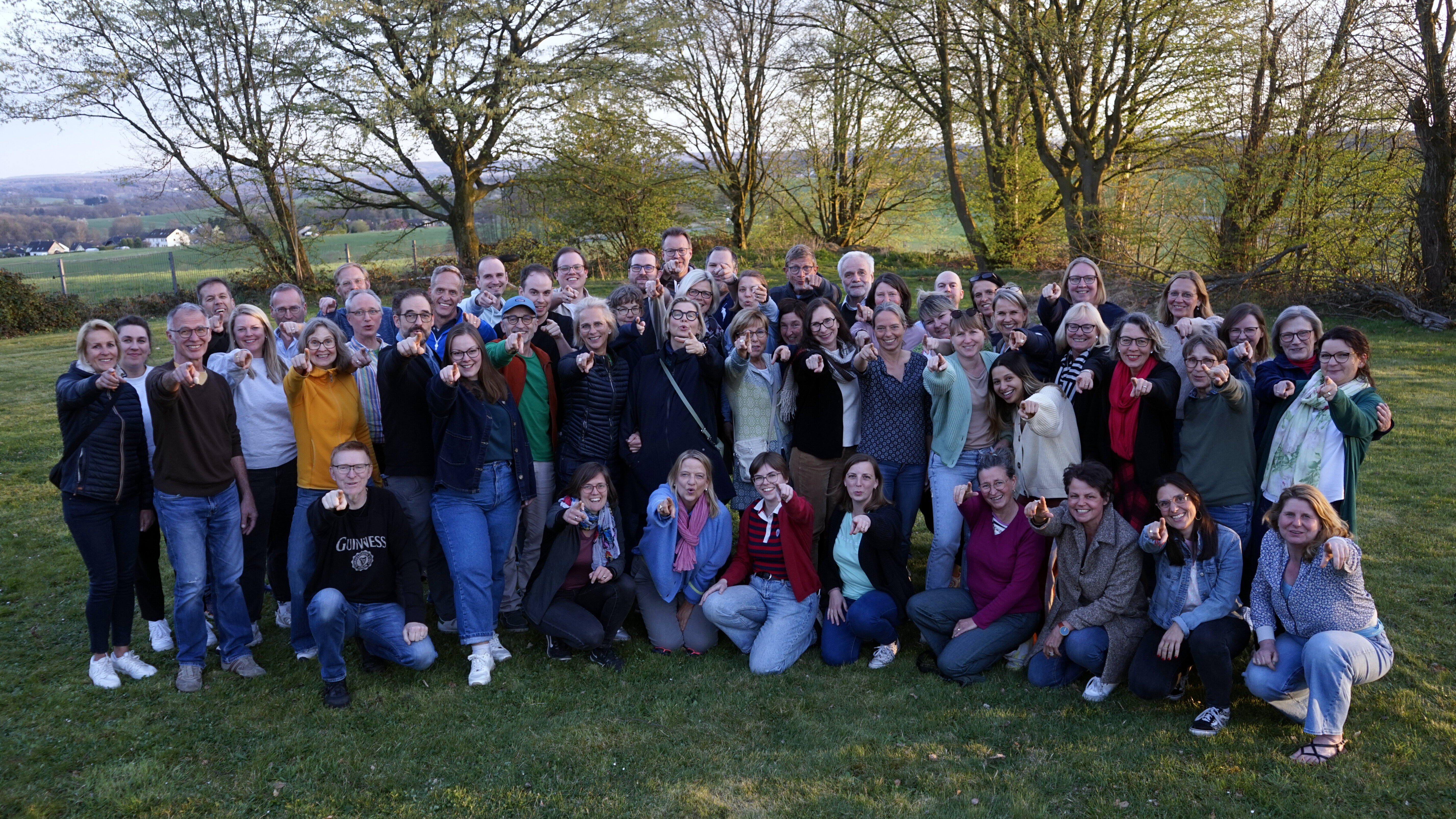 Im Hintergrund Bäume, im Vordergrund der Querbeat-Chor auf einer grünen Wiese, alle zeigen in die Kamera