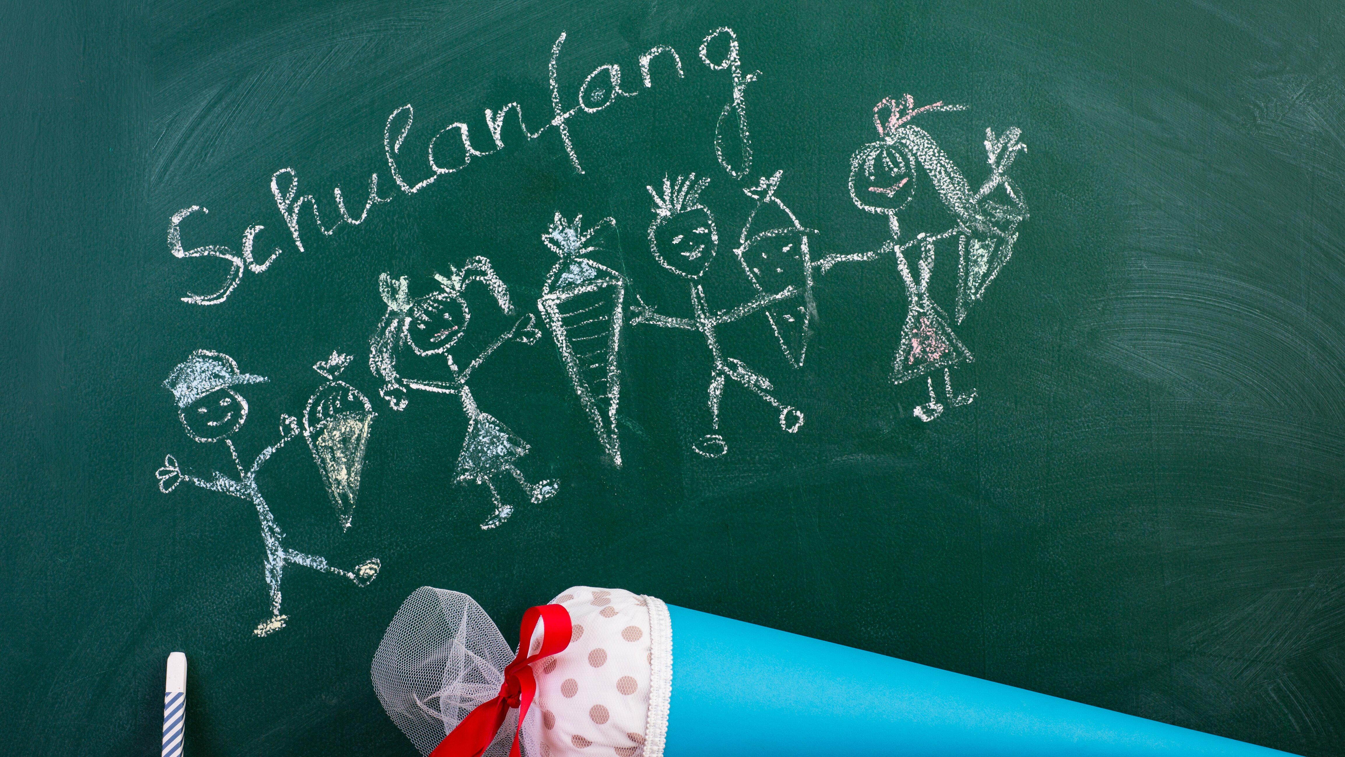 Blaue Schultüte liegt vor einer Kreidetafel auf der der Schriftzug Schulanfang zu lesen ist