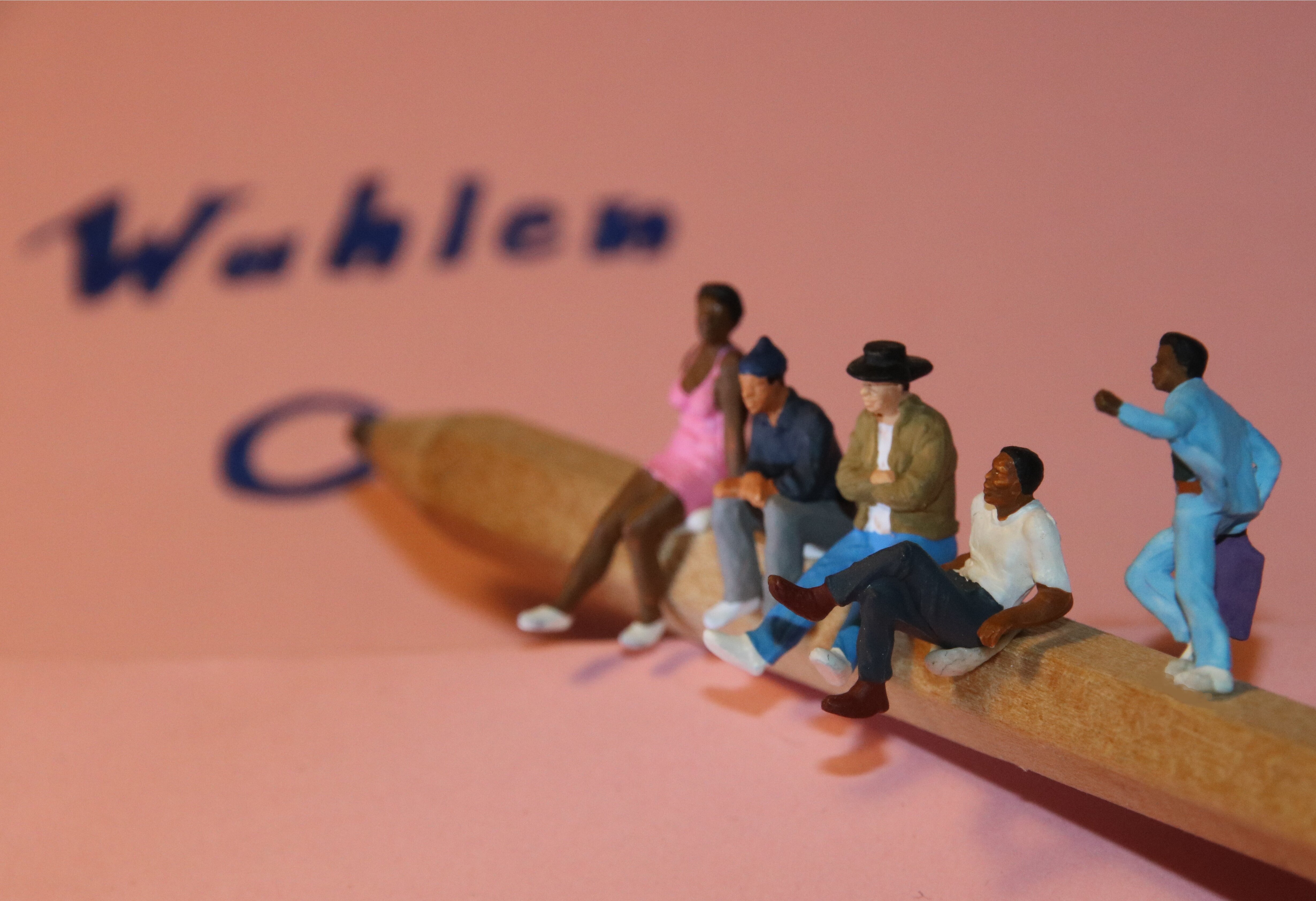 Figürliche Darstellung von Migrantinnen und Migranten auf einem großen Bleistift, die einen Wahlzettel ankreuzen, © Stadt Köln/Timm Therre