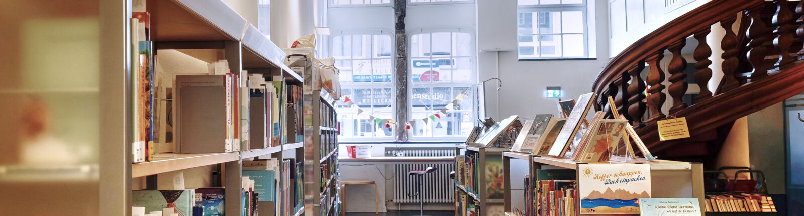 Innenraum der Statteilbibliothek Haus Balchen, links sind Bücherregale, rechts eine historische Holztreppe, © Stadtbibliothek Köln