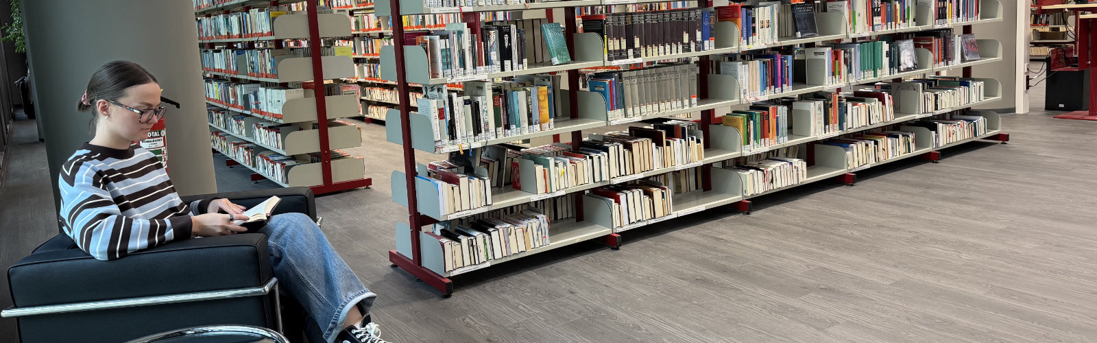Frau sitzt lesend im Sessel neben Bücherregalen im Interim der Stadtbibliothek 