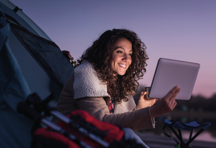 Frau mit Tablet beim Zelten im Abendlicht, © iStock.com/vladans