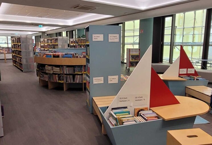 Zwei Segelboote aus Holz mit Kinderbüchern gefüllt sowie verschiedene Regale mit Kinderbüchern, © Stadtbibliothek Köln