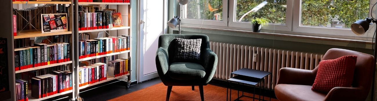 Leseecke mit zwei Sesseln vor Fensterfront und Beistelltisch dazwischen, links ein Bücherregal, © Stadtbibliothek Köln