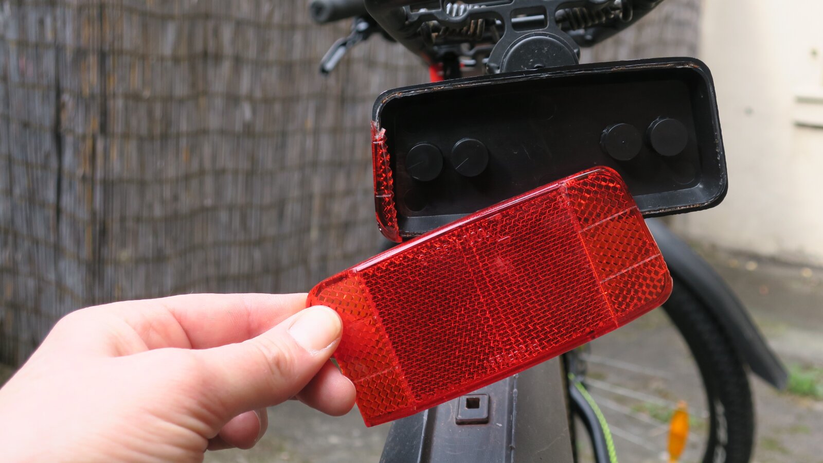 Eine Hand hält ein zerbrochens Teil ein Fahrradrückstrahler hoch. Das Fahrrad steht im Hintergrund., &copy Stadt Köln