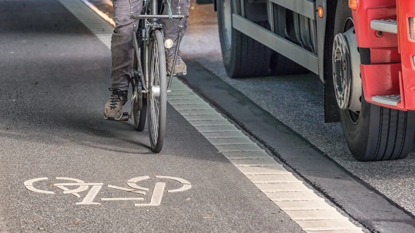 Zu sehen ist ein Radfahrernder auf einem Radfahrstreifen, rechts daneben ein Lastkraftwagen.