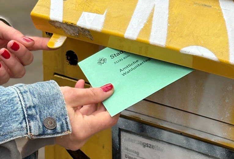 Grüner Briefwahlumschlag wird in Deutsche-Post-Briefkasten geworfen, © Stadt Köln